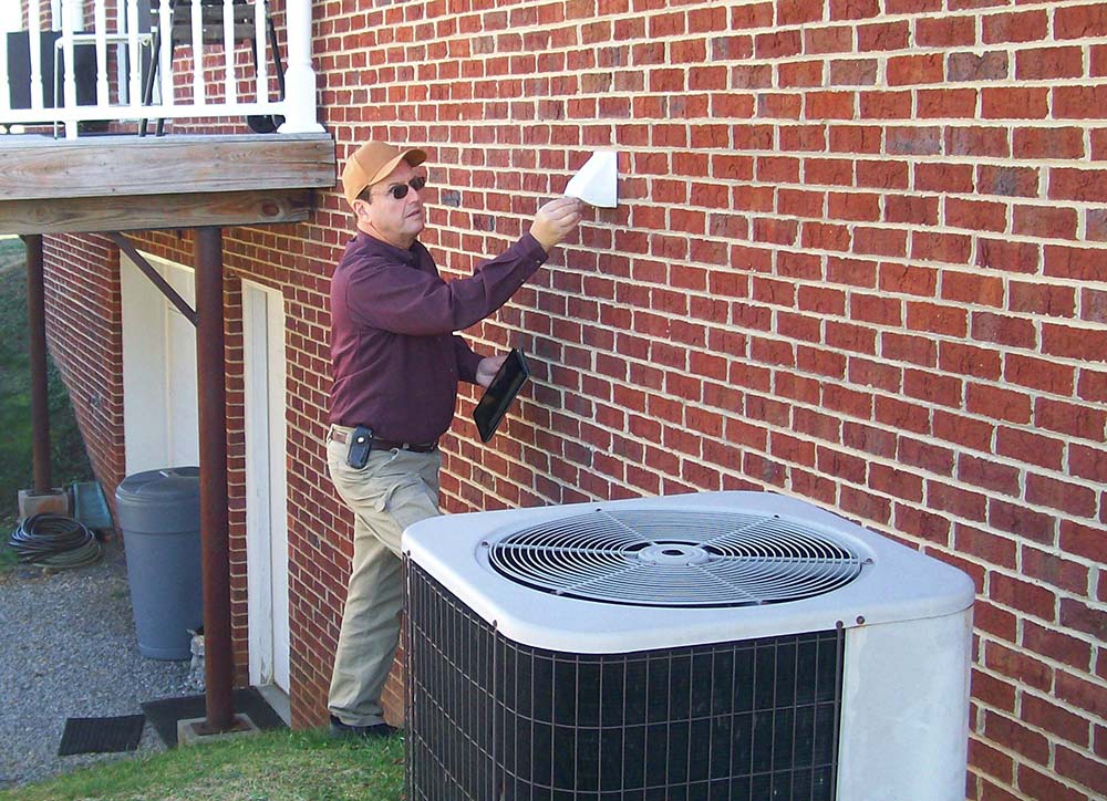 Bill Rupert, one of Tennessee's licensed home inspectors, examining the exterior of a brick house and air conditioning system