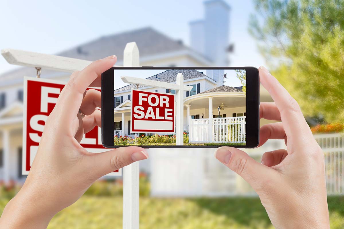 Hands holding up a smartphone and taking pictures of a house for sale after passing thorough pre-listing home inspection services