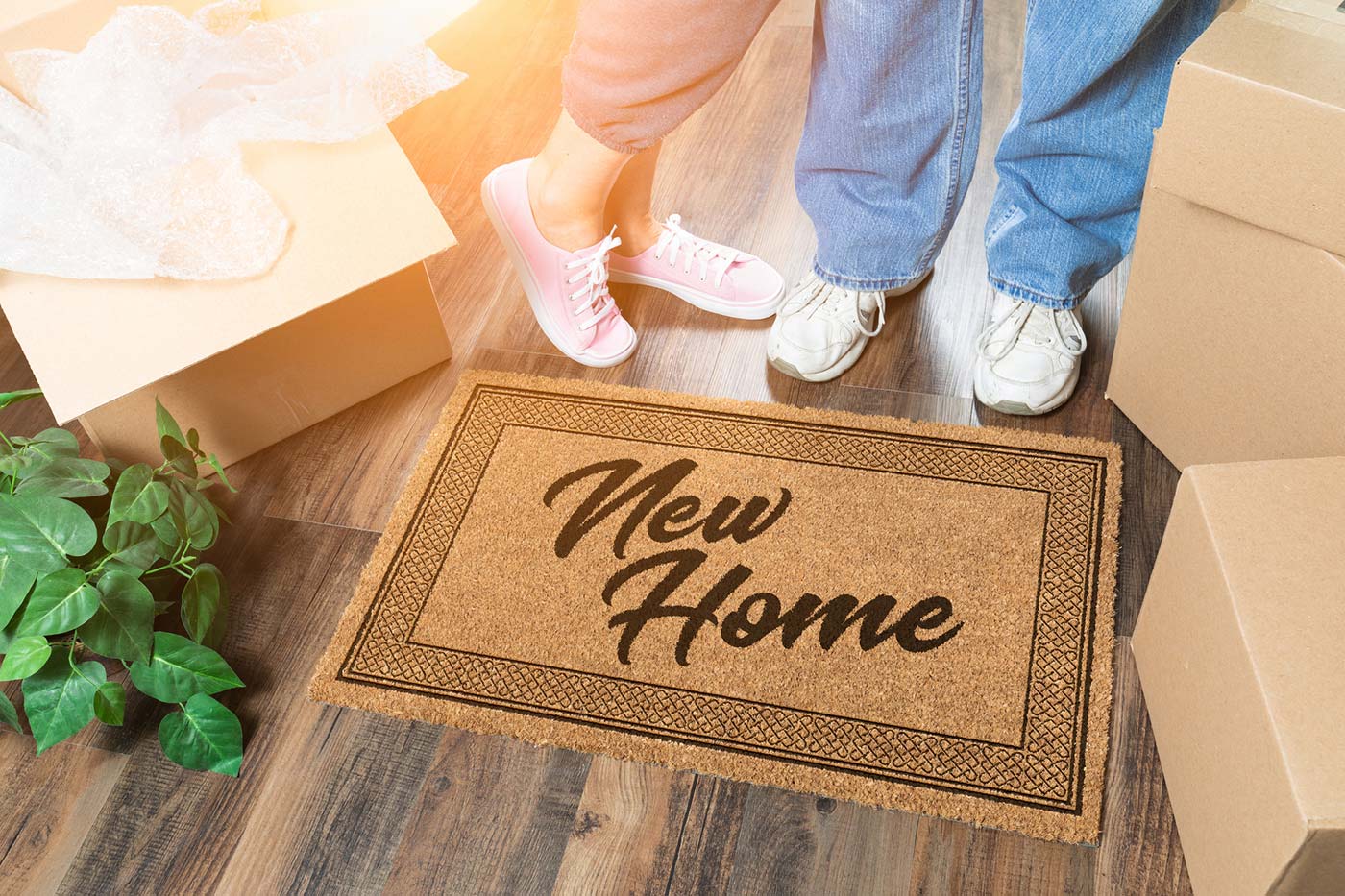 A couple standing next to a New Home welcome mat and moving boxes after receiving thorough home inspection services